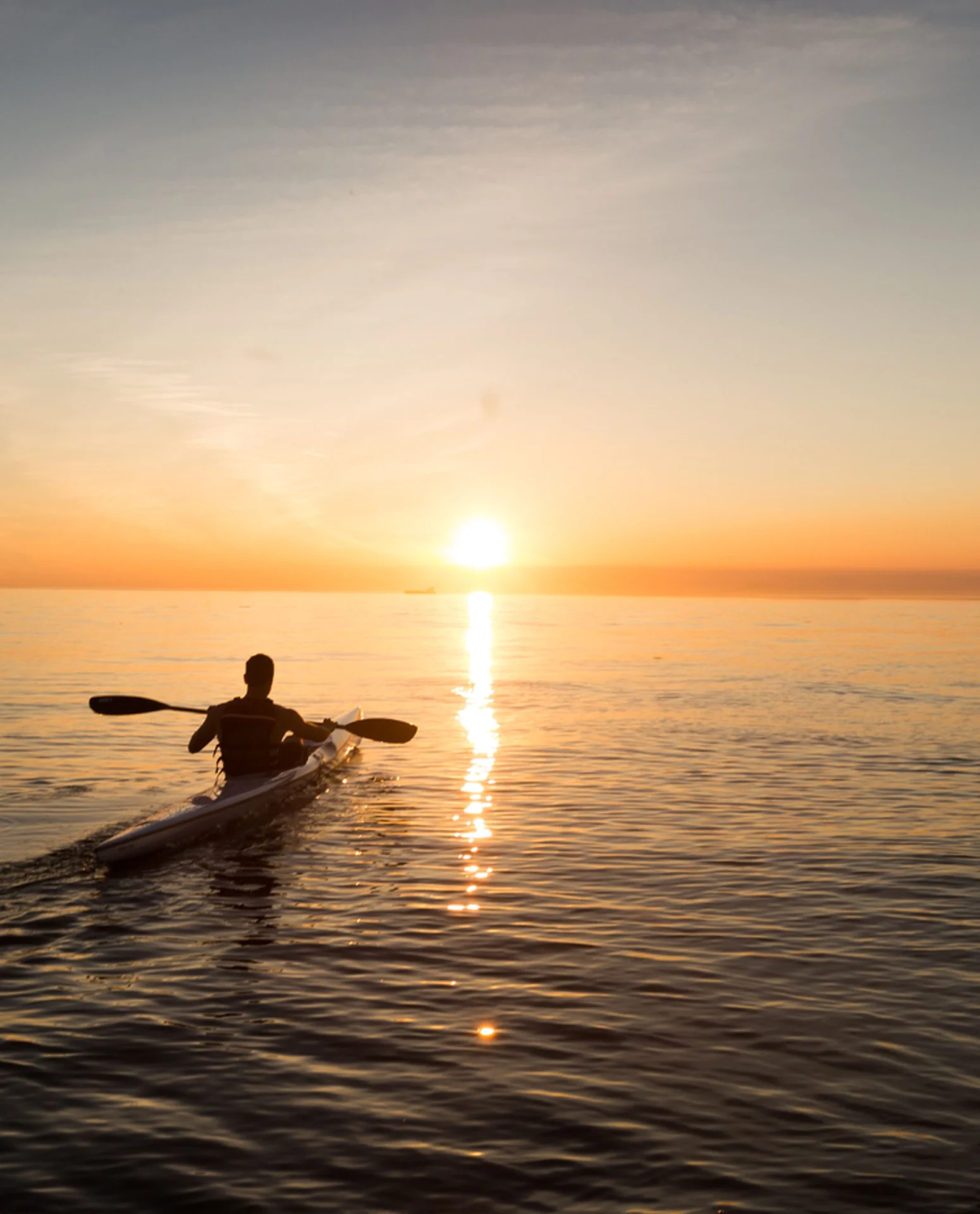 A person in a kayak on the ocean at sunset.