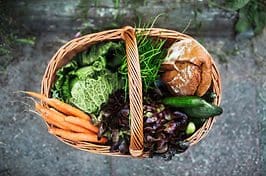 A basket full of vegetables and bread on the ground.