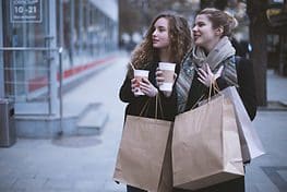 Two women walking down a street holding coffee.