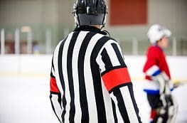 A referee is standing on the ice with his arm around him.