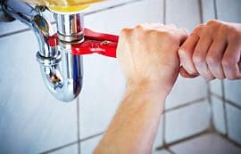 A person holding a pair of red handled pliers over the faucet.