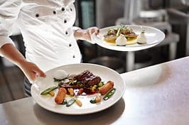 A chef is holding two plates of food.