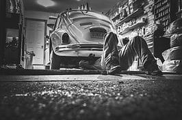 A person is sitting on the floor in front of an old car.